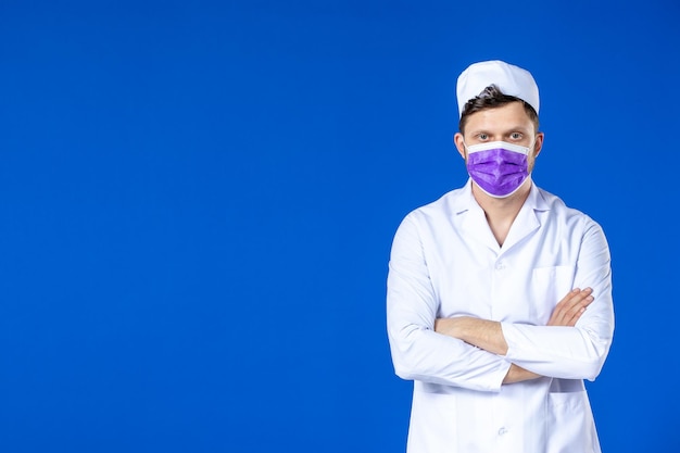 Vista frontale del medico maschio in tuta medica e maschera viola sull'azzurro