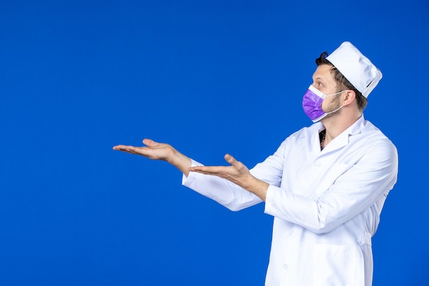 Vista frontale del medico maschio in tuta medica e maschera viola sull'azzurro