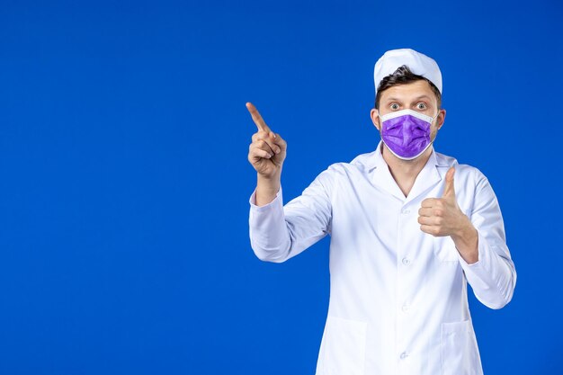 Vista frontale del medico maschio in tuta medica e maschera viola sull'azzurro