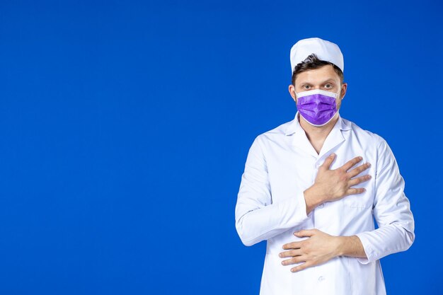 Vista frontale del medico maschio in tuta medica e maschera viola sull'azzurro