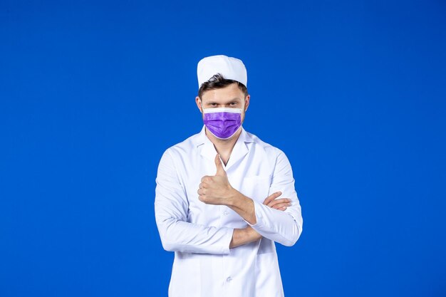 Vista frontale del medico maschio in tuta medica e maschera viola sull'azzurro