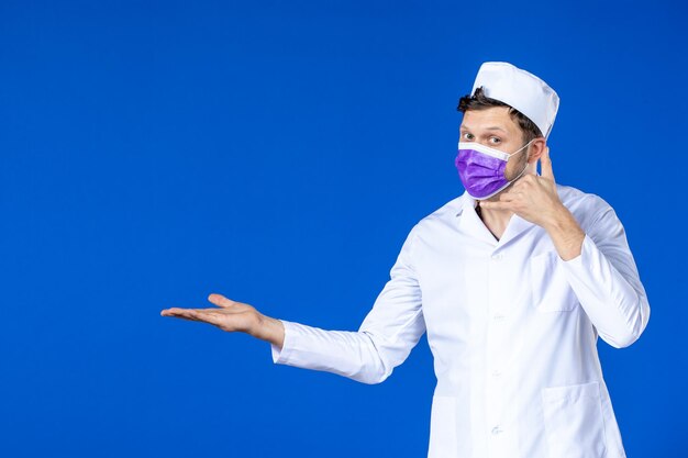 Vista frontale del medico maschio in tuta medica e maschera viola sull'azzurro