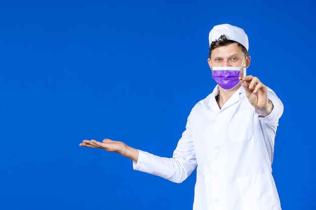 Vista frontale del medico maschio in tuta medica e maschera viola tenendo l'iniezione sull'azzurro