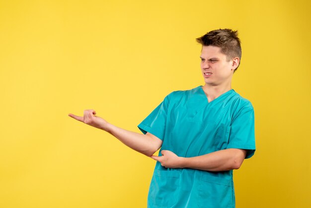 Vista frontale del medico maschio in tuta medica sulla parete gialla