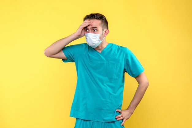 Vista frontale del medico maschio scioccato e spaventato muro giallo