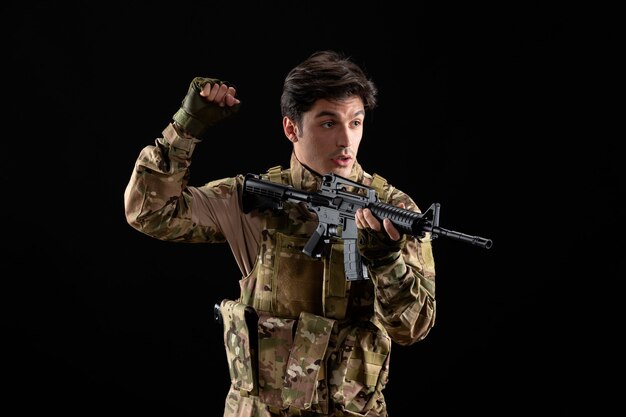 Vista frontale del militare in uniforme che punta il suo fucile in studio sulla scrivania nera