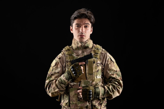 Vista frontale del militare in uniforme che tiene la pistola sul muro nero