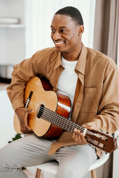 Vista frontale del musicista maschio di smiley a casa a suonare la chitarra