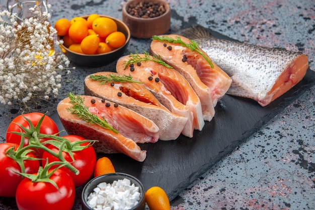 Vista frontale del pesce crudo tagliato fresco verde sul vassoio di colore scuro spezie kumquat bottiglia di olio sulla tabella dei colori della miscela nera blu