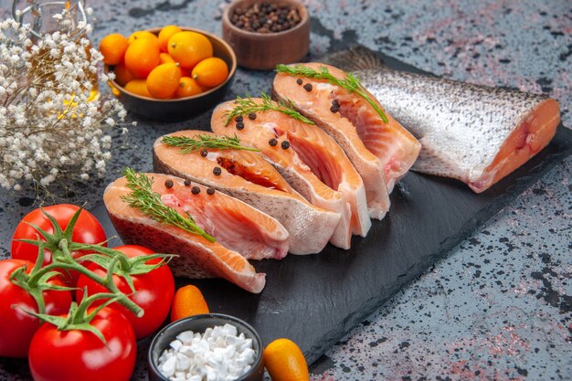 Vista frontale del pesce crudo tagliato fresco verde sul vassoio di colore scuro spezie kumquat bottiglia di olio sulla tabella dei colori della miscela nera blu