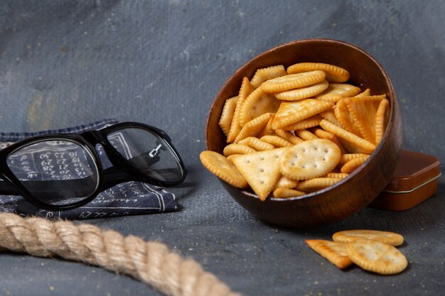 Vista frontale del piatto marrone con cracker salati e occhiali da sole