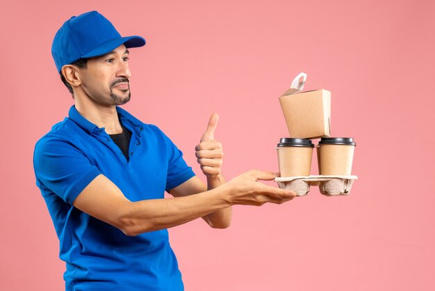 Vista frontale del ragazzo delle consegne maschio emotivo pazzo che indossa un cappello che tiene gli ordini facendo un gesto ok