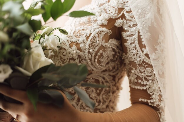 Vista frontale del ricamo sul corsetto del vestito da sposa e bouquet da sposa di eustomas bianchi