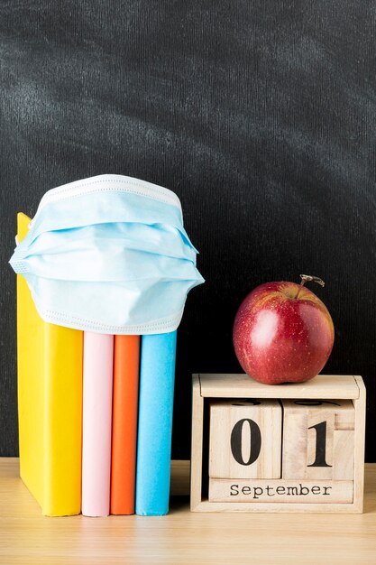 Vista frontale del ritorno a materiale scolastico con maschera medica e libri