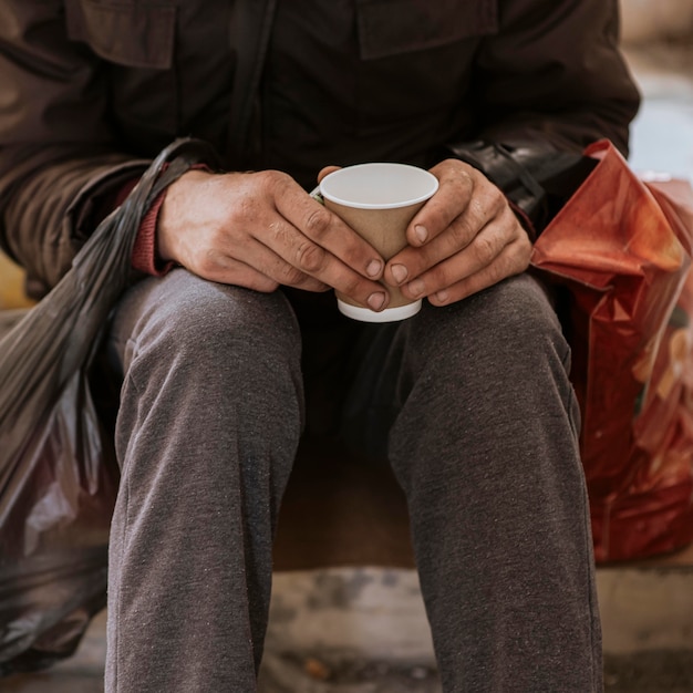 Vista frontale del senzatetto che tiene tazza e sacchetto di plastica