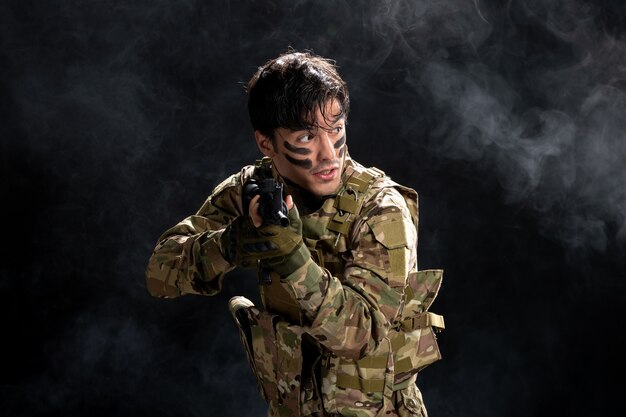 Vista frontale del soldato maschio che combatte in mimetica con il fucile sul muro nero
