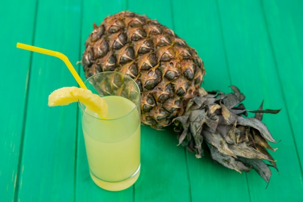 Vista frontale del succo di ananas con ananas su superficie verde