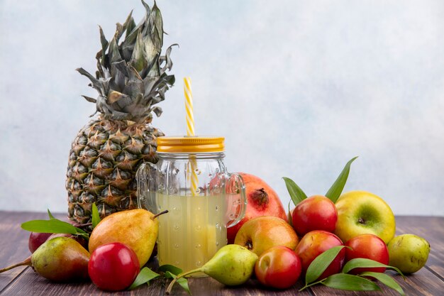 Vista frontale del succo di ananas con i frutti come melograno della mela della prugna della pesca dell'ananas su superficie di legno e superficie bianca