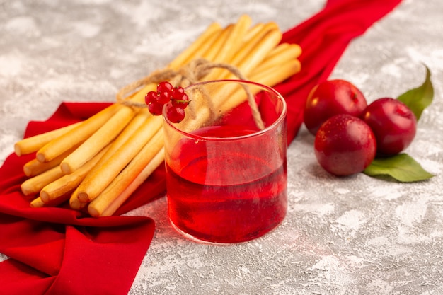 Vista frontale del succo di prugna con prugne fresche e cracker stick su frutta bianca color vitamina estate