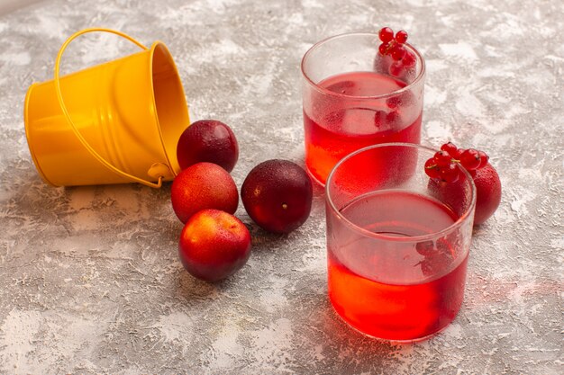 Vista frontale del succo di prugna rosso colorato con prugne fresche su grigio