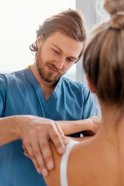 Vista frontale del terapista osteopatico che controlla la spalla del paziente femminile