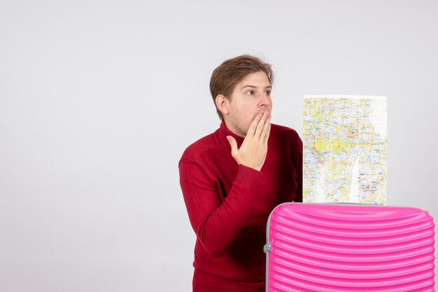 Vista frontale del turista maschio con mappa e borsa rosa sul muro bianco