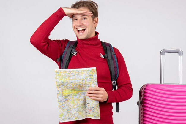 Vista frontale del turista maschio con zaino e mappa sul muro bianco