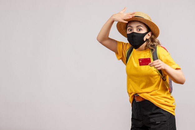 Vista frontale del viaggiatore femminile sveglio con lo zaino che sostiene la carta sul muro grigio