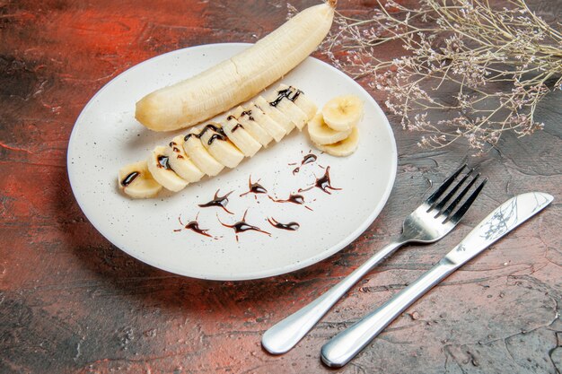 Vista frontale deliziosa banana con pezzi affettati all'interno del piatto su uno sfondo scuro dolce foto albero colore frutta