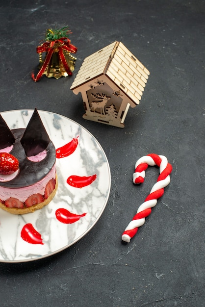 Vista frontale deliziosa cheesecake con fragole e cioccolato su giocattoli di albero di natale piatto ovale su sfondo scuro dark