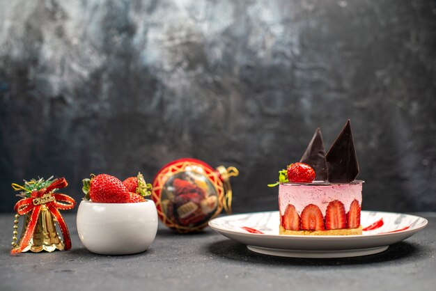 Vista frontale deliziosa cheesecake con fragole e cioccolato su piatto ovale ciotola di fragole giocattoli di natale