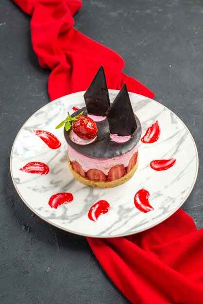 Vista frontale deliziosa cheesecake con fragole e cioccolato su piatto scialle rosso su oscurità
