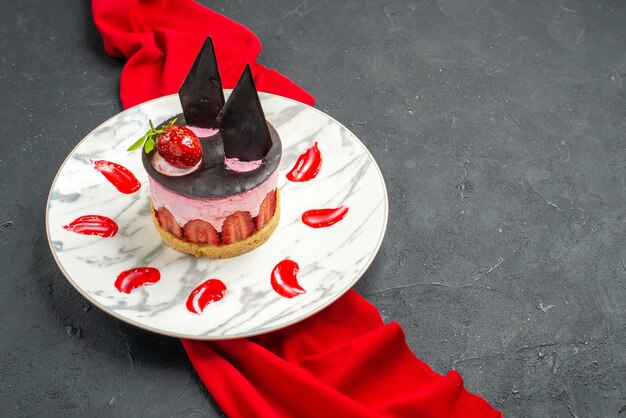Vista frontale deliziosa cheesecake con fragole e cioccolato su piatto scialle rosso su sfondo scuro isolato posto libero