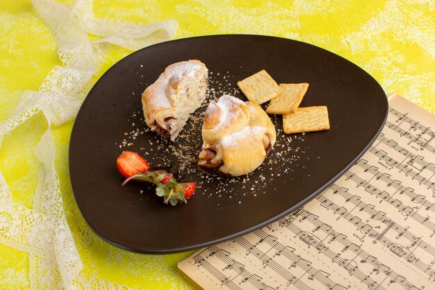 Vista frontale deliziosa pasticceria all'interno del piatto marrone con cracker sul tavolo giallo, cuocere la pasticceria dolce alla frutta del tè