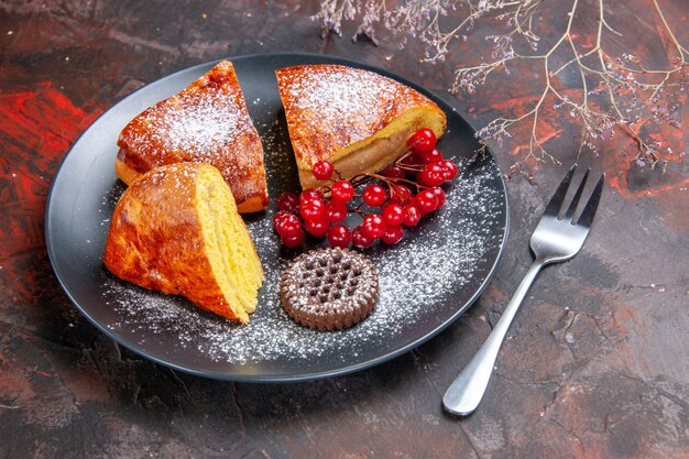 Vista frontale deliziosa torta a fette con bacche rosse sul pavimento scuro