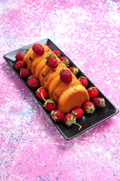 Vista frontale deliziosa torta al forno all'interno della tortiera nera con fragole rosse fresche sulla scrivania rosa.