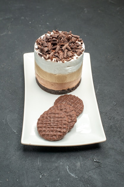 Vista frontale deliziosa torta con cioccolato e biscotti su piatto rettangolare bianco su oscurità