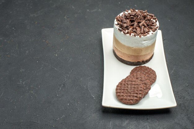 Vista frontale deliziosa torta con cioccolato e biscotti su piatto rettangolare bianco su spazio libero scuro