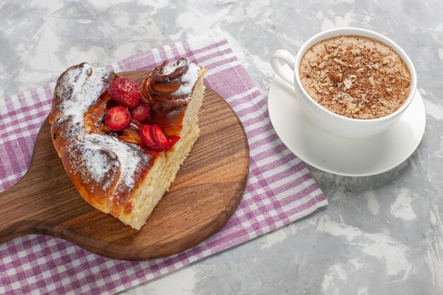 Vista frontale deliziosa torta di fragole al forno e gustosa fetta di dessert con una tazza di caffè sulla scrivania bianca