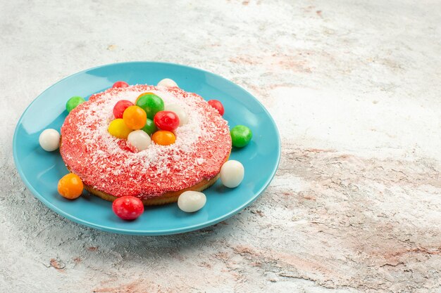 Vista frontale deliziosa torta rosa con caramelle colorate all'interno del piatto su fondo bianco torta color arcobaleno dolce caramelle