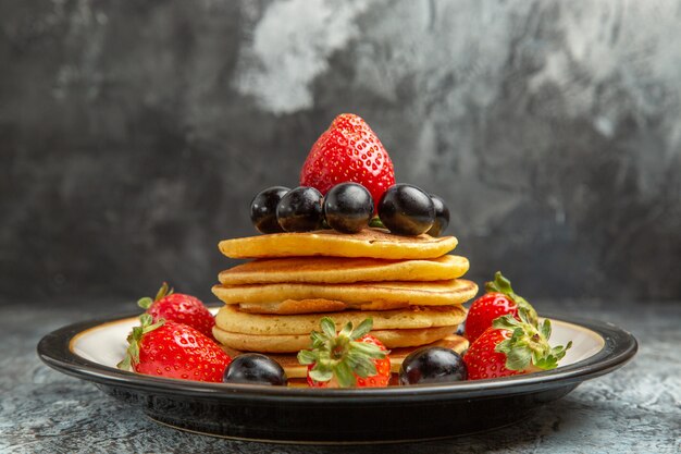 Vista frontale deliziose frittelle con frutta e bacche sul dessert torta di frutta superficie scura