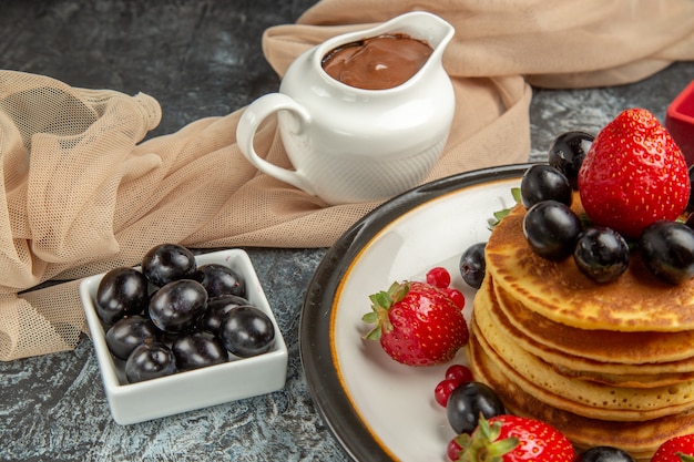 Vista frontale deliziose frittelle con frutta e bacche sulla torta di frutta superficie leggera dolce