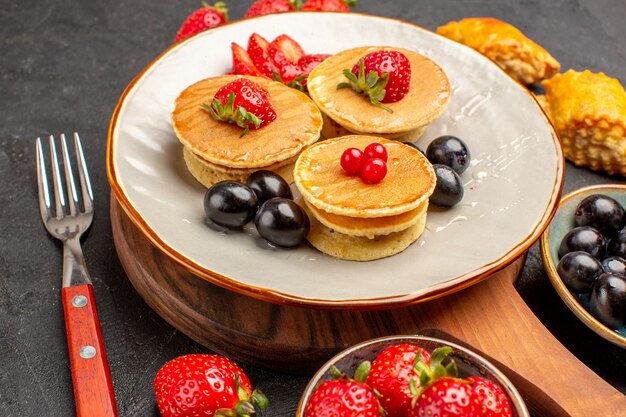 Vista frontale deliziose frittelle con frutta sulla torta di superficie scura torta dolce di frutta