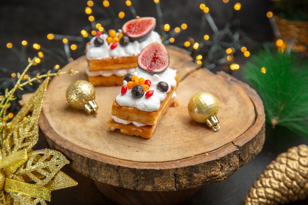 Vista frontale deliziose torte alla crema intorno ai giocattoli dell'albero di capodanno su sfondo scuro torta dolce crema fotografica dessert