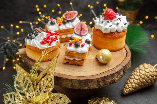 Vista frontale deliziose torte alla crema intorno ai giocattoli dell'albero di capodanno su una torta da scrivania scura dolce crema fotografica dessert