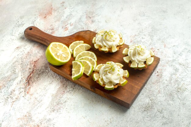 Vista frontale deliziose torte cremose con fette di limone su superficie bianca torta biscotto biscotto crema dolce tè