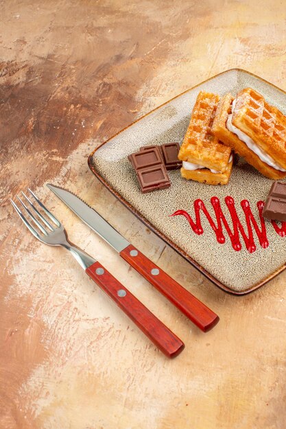 Vista frontale deliziose torte di waffle con barrette di cioccolato sulla scrivania marrone