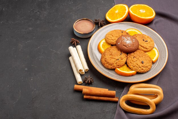 Vista frontale deliziosi biscotti con arance fresche affettate sullo sfondo scuro biscotto di zucchero biscotto di frutta dolce