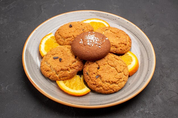 Vista frontale deliziosi biscotti di zucchero con arance a fette all'interno del piatto sullo sfondo scuro biscotto di zucchero biscotto dolce frutta