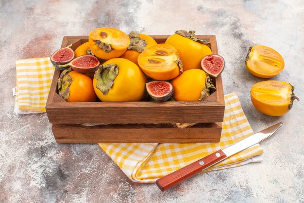 Vista frontale deliziosi cachi e fichi tagliati in una scatola di legno asciugamano da cucina giallo un coltello su sfondo nudo